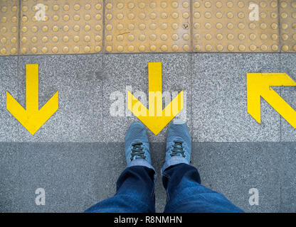 Blick von oben auf die Mann stehend über das Pfeilsymbol auf u-Plattform. Gelber Pfeil auf dem Boden am Bahnhof. Stockfoto