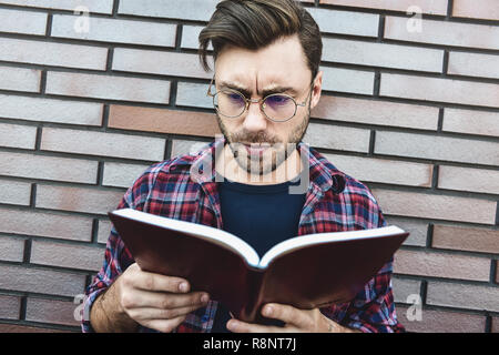 Portrait von lächelnden stattlicher Mann in runde Gläser und Shirt isoliert auf braun Mauer. Stockfoto