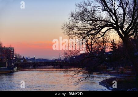 Elgin, Illinis, USA. Leuchtet auf, entlang der Straßen und Brücken, die die Fox River in der Abenddämmerung überholt in der Stadt am Fluss Sonnenuntergang. Stockfoto