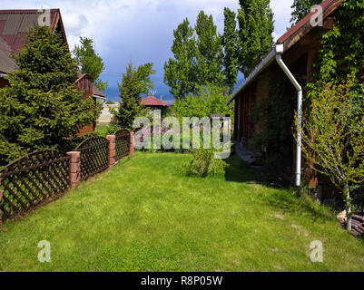 Luxuriöse, moderne Holz Abstellgleis home Exterieur. Schönen Hinterhof Landschaft mit gepflegten Rasen, Blumenbeeten und Holzzaun. Stockfoto