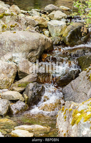Das Wasser fällt über große Felsen und kleinen Steinchen Stockfoto