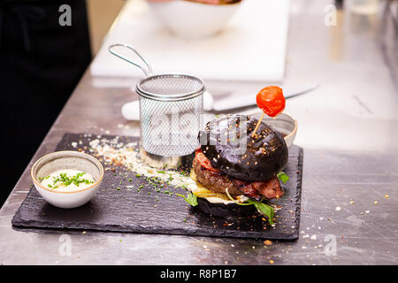 Schwarz Burger mit Pommes frites auf Stein Schneidebrett. In der Küche Restaurant Stockfoto