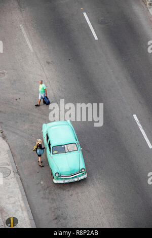 Aus der Vogelperspektive eines alten, türkisfarbenen Autos aus den 1950er Jahren, das auf einer Straße geparkt ist, und zwei Fußgänger, die daneben in Havanna Kuba spazieren Stockfoto