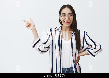 Gisl zeigen auf großer Platz, gerade um die Ecke und bittet Freund Kaffee trinken und plaudern. Portrait von glücklich gut aussehende weibliche Geschäftsfrau in Ohrringe und Gläser, die Hand auf die Hüfte und Übersicht Links Stockfoto