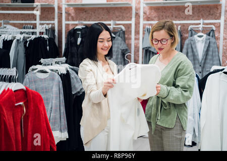 Sales Consultant helfen wählt Kleidung für den Kunden in der Filiale. Shopping mit Stylistin Konzept. Weibliche Verkäufer und junge Frau in der Modeboutique Stockfoto