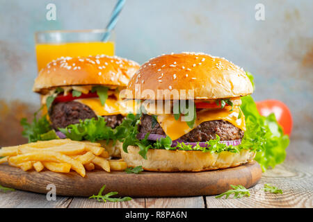 Zwei frische hausgemachte Burger mit Bratkartoffeln und Orangensaft auf einem Tisch Stockfoto