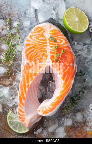 Rohe frische Lachs oder Forelle Steak auf Eis, die reich an Omega-3-Öl, mit Kalk, Thymian und Olivenöl auf einem blauen Hintergrund rostig. Gesunde Ernährung Lebensmittel. Ansicht von oben. Flach Stockfoto