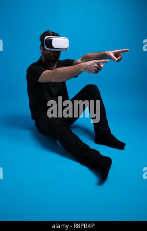 Männliche unten stehend und das Tragen der VR-Gerät zeigt zwei Hand Finger zur Seite. Studio geschossen von jungen männlichen genießen Technologie Stockfoto