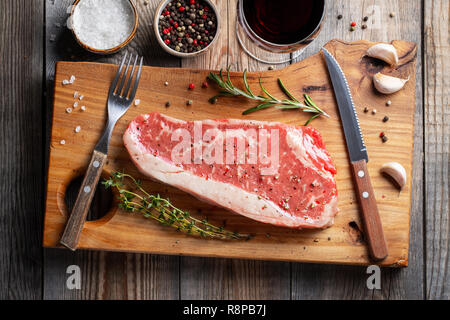 Frische rohe Prime Black Angus Beef Steaks mit Gewürzen und Rotwein auf dem Holzbrett: Roastbeef, Rib Eye. Ansicht von oben. Auf einem dunklen rustikalen Tisch Stockfoto