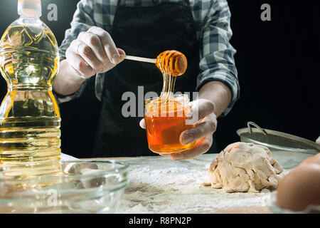 Professionelle männlichen Cook streusel Teig mit Mehl, preapares oder backt Brot oder Nudeln am Küchentisch, hat dreckige Uniform, über Schwarze Kreide Hintergrund isoliert. Backen Konzept Stockfoto