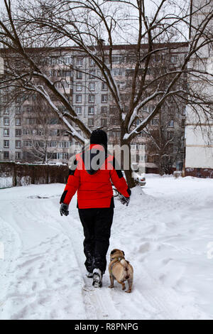 Junge Spaziergänge mit Hund an einem Wintertag. Jugendlicher und Mops auf einer Straße der Stadt. Stockfoto