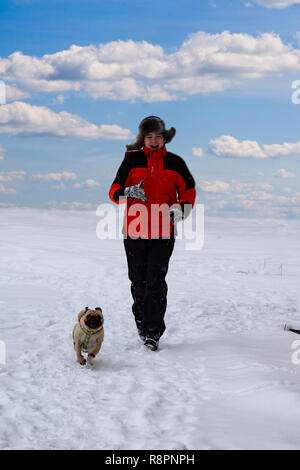 Junge Spaziergänge mit Hund an einem Wintertag. Teenager und pug laufen im Schnee gegen den Himmel.