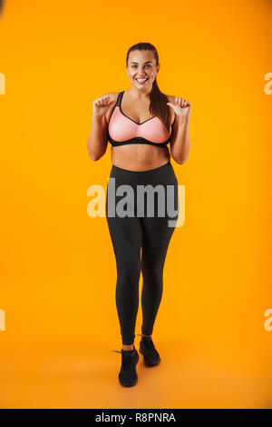 In voller Länge Porträt einer fröhlichen Übergewicht fitness Frau tragen Sport Kleidung, die auf gelben Hintergrund isoliert Stockfoto