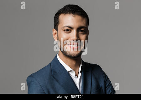 Bild des erfolgreichen arabischer Geschäftsmann 30 s im Anzug an Kamera lächelnd über grauer Hintergrund Stockfoto