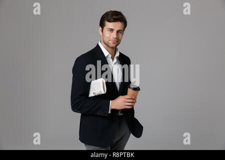 Bild Der unrasierte Mann 30 s in sachlich Anzug hält Kaffee und Zeitung isoliert über grauer Hintergrund Stockfoto