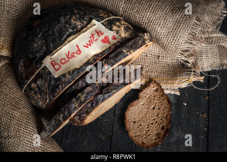 Crusty Deutschen braun Brot und Gebäck mit liebe Nachricht auf eine Variable, die auf eine Jute Sack. Gesundes Roggenbrot. Oben Blick auf Ernährung Brot. Hausgemachte Grundnahrungsmittel. Stockfoto