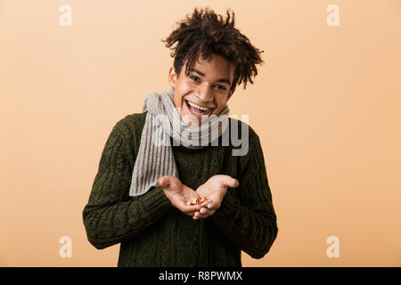 Portrait eines glücklichen jungen afrikanischen Mann im Herbst Kleidung über beigen Hintergrund isoliert gekleidet, mit Pillen Kapseln Stockfoto