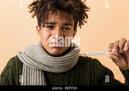 Nahaufnahme, Porträt einer jungen afrikanischen Mann im Herbst Kleidung über beigen Hintergrund isoliert gekleidet, holding Thermometer Stockfoto