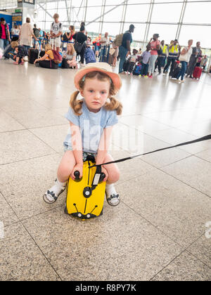 Vier Jahre altes Kind am Flughafen sitzen auf ihren kleinen Koffer Trunki müde Stockfoto
