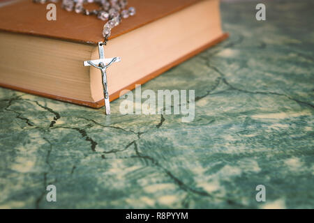 Silber Rosenkranz und Kreuz ruht auf das geschlossene Buch am grünen Tisch, Vorderansicht. religion Schule Konzept. Vintage Style. Stockfoto