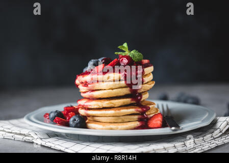 Pfannkuchen mit Beeren Sauce und Beeren auf dunklem Hintergrund. Pfannkuchen mit Heidelbeeren, Erdbeeren und süßen Soße Stapel. Detailansicht Stockfoto