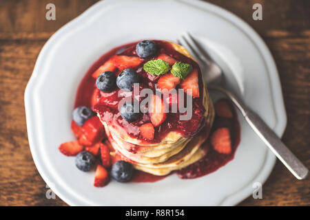 Pfannkuchen mit süßen Beeren-Sauce und frische Beeren auf einem Teller mit frischen Heidelbeere, Erdbeere, Minze Blatt. Table Top Aussicht, Nahaufnahme, getönten Bild Stockfoto