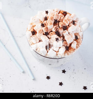 Heiße Schokolade oder Kakao mit Schlagsahne und Marshmallow candy bestreut mit Zimt oder Kakao Pulver mit Schokolade Sterne auf weißem Marmor tisch und Stockfoto