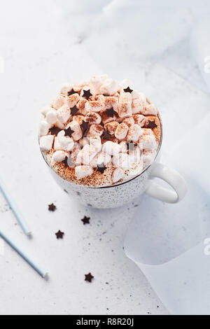 Heiße Schokolade oder Kakao mit Schlagsahne und Marshmallow candy bestreut mit Zimt oder Kakao Pulver mit Schokolade Sterne auf weißem Marmor tisch und Stockfoto