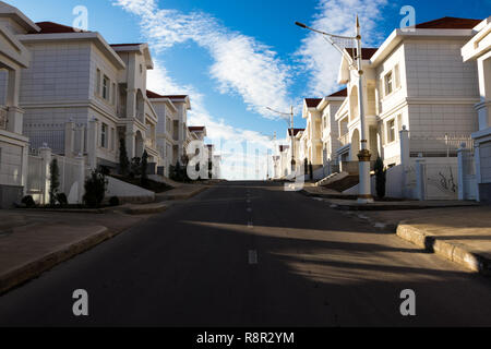 Wohnviertel, weiße Häuser mit roten Dächern auf einem Hintergrund von einem blauen bewölkten Himmel. Immobilien und Grundstücke Stockfoto