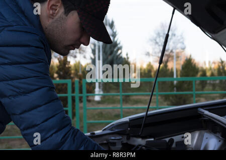 Nahaufnahme, Porträt eines jungen Mannes in die Reparatur einer kaputten Auto im Freien an einem Parkplatz am Mittag. Notdienst. Stockfoto