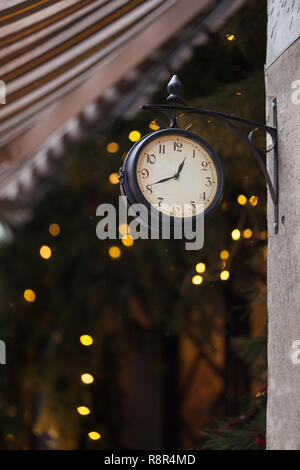 Vintage Doppelseitige Wanduhr auf einem Hintergrund von hellen Lichtern. Urlaub Frohes neues Jahr festliche Konzept. Wanduhr mit arabischen Ziffern und einem weißen Stockfoto
