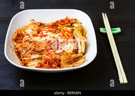 Die koreanische Küche - kimchi Vorspeise (würzige nappa Kohl) in Weiß Schüssel und Essstäbchen auf dunkelbraunen hölzernen Tisch Stockfoto