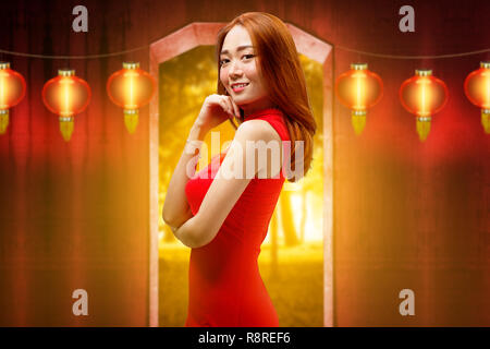 Gerne chinesische Frau mit traditionellen Kleidung gegen die Laternen auf dem Hintergrund posiert. Happy Chinese New Year Stockfoto