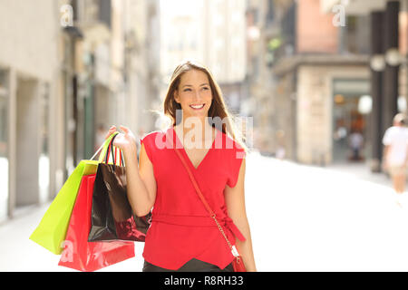 Vorderansicht Portrait Of Happy Shopper zu Fuß in Richtung Kamera holding Einkaufstüten auf der Straße einer alten Stadt Stockfoto