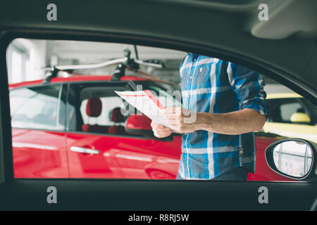 Perfekte Linien. Die junge Dunkelhaarige bärtiger Mann Prüfung Auto im Autohaus und seine Wahl. Horizontale Porträt einer jungen Kerl am Auto. Er überlegt, ob er es kaufen sollte. Stockfoto