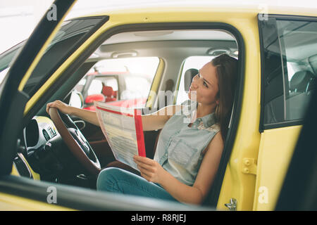 Schöne junge Frau ein Auto kaufen beim Händler. Weibliche Modell sitzen sitzt in den Innenraum Stockfoto