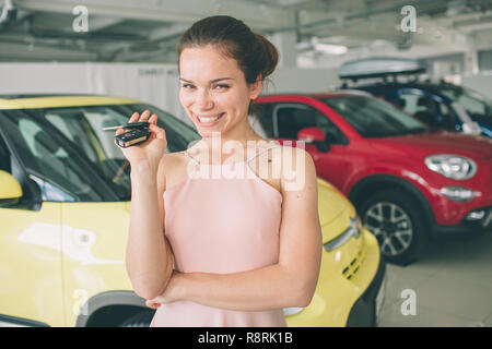 Schöne junge Frau hält ein Schlüssel im Autohaus. Stockfoto