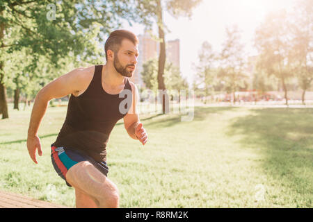 Athletischen jungen Mann in der Natur zu laufen. Gesunde Lebensweise. Bärtige schwarzhaarige Sportler läuft auf der Straße - Sonnenuntergang zurück lit Stockfoto