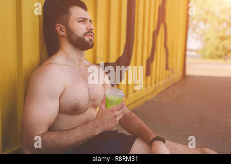 Hübscher junger muskulöser Mann Getränke Grün detox Smoothie Cup. Bild eines jungen athletischen Mann nach dem Training. Stockfoto