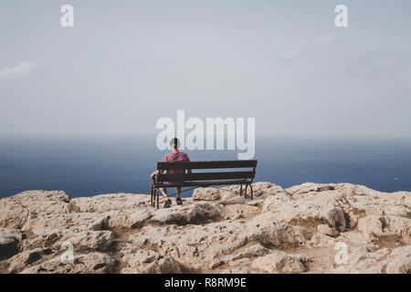 Rentner, die auf einer Bank sitzen und auf das Meer. Alte älterer Mann sitzt alleine auf einer Bank auf einem Felsen und in die Ferne schaut. Konzept der Einsamkeit Stockfoto