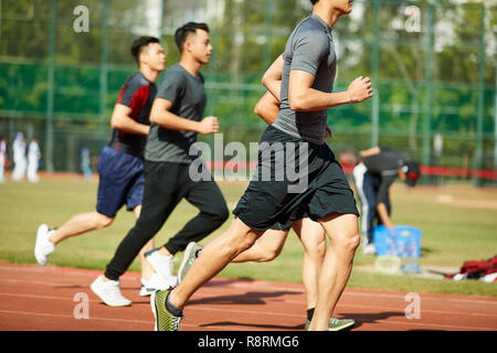Vier jungen asiatischen Leichtathleten racing gegeneinander konkurrieren. Stockfoto