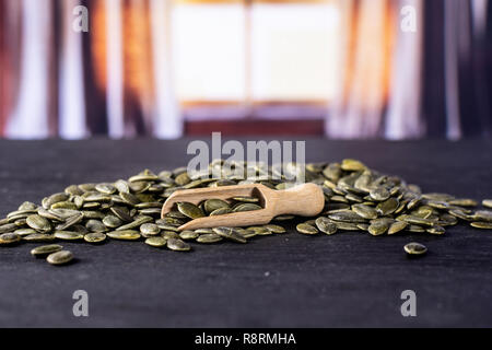 Menge ganze geschälte Kürbiskerne mit Holz- Schaufel mit seidenen Vorhängen hinter Stockfoto