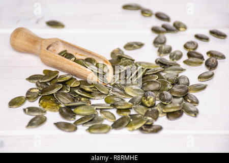 Menge ganze geschälte Kürbiskerne mit Holz- Schaufel auf weißem Holz Stockfoto