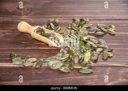 Menge ganze geschälte Kürbiskerne mit Holz- Schaufel auf braunem Holz Stockfoto