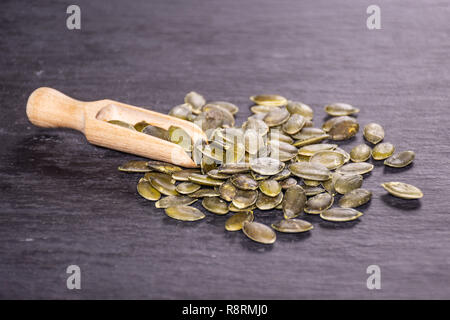 Menge ganze geschälte Kürbiskerne mit Holz- Schaufel auf grauem Stein Stockfoto