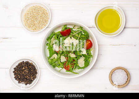 Das Mischen von Zutaten Schritt. Rezept Schritt für Schritt Rucola Salat in einem grauen Keramik Schüssel flatlay auf weißem Holz Stockfoto