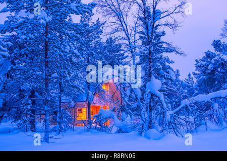 Winter im finnischen Lappland. Das Licht einer einsamen Hütte in den dichten Wald am Abend. Viel Schnee Stockfoto