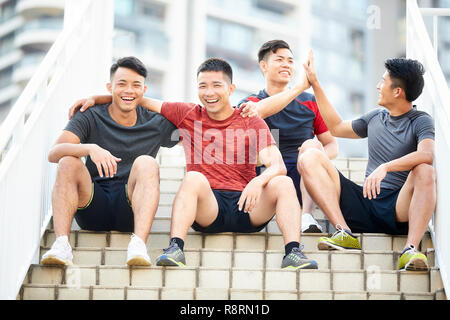 Gruppe von vier glückliche junge asiatische männliche Athleten sitzen auf Schritte entspannend Stockfoto