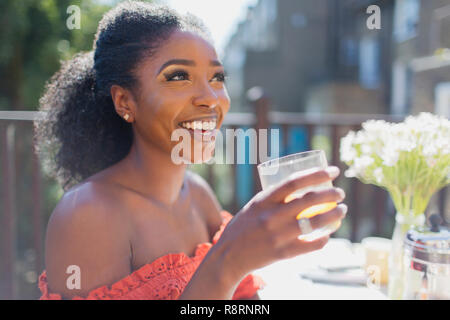 Glückliche junge Frau trinkt Orangensaft auf sonnigen Balkon Stockfoto