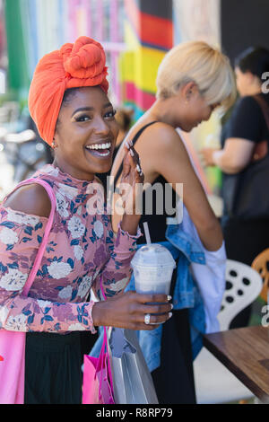 Portrait glückliche, unbeschwerte junge Frau mit Kopftuch trink Smoothie Stockfoto